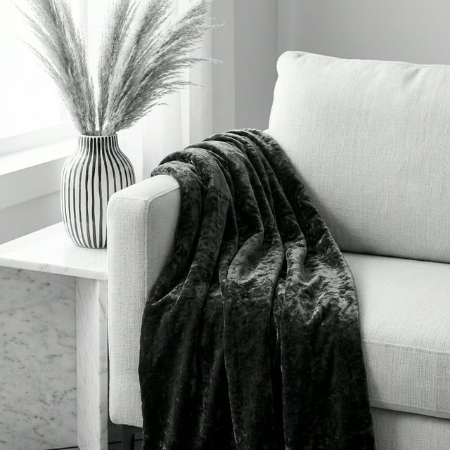 Layered textures in a black and white room: velvet throw on linen chair with ceramic vase